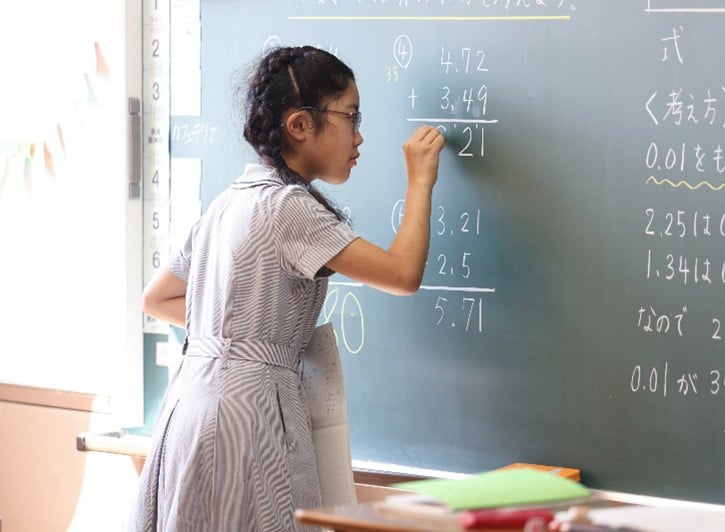 黒板に算数の答えを書いている女子生徒の写真